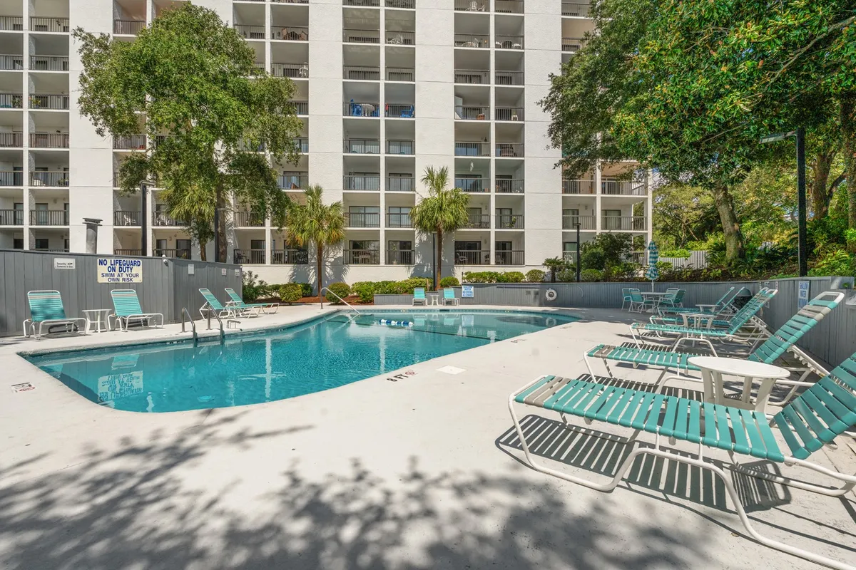 This image captures a beautifully maintained outdoor swimming pool surrounded by lounge chairs and tall palm trees. The setting is sunny and inviting, with plenty of space for guests to relax, swim, or socialize. The overall mood is leisurely and carefree, evoking the essence of a resort-style getaway.