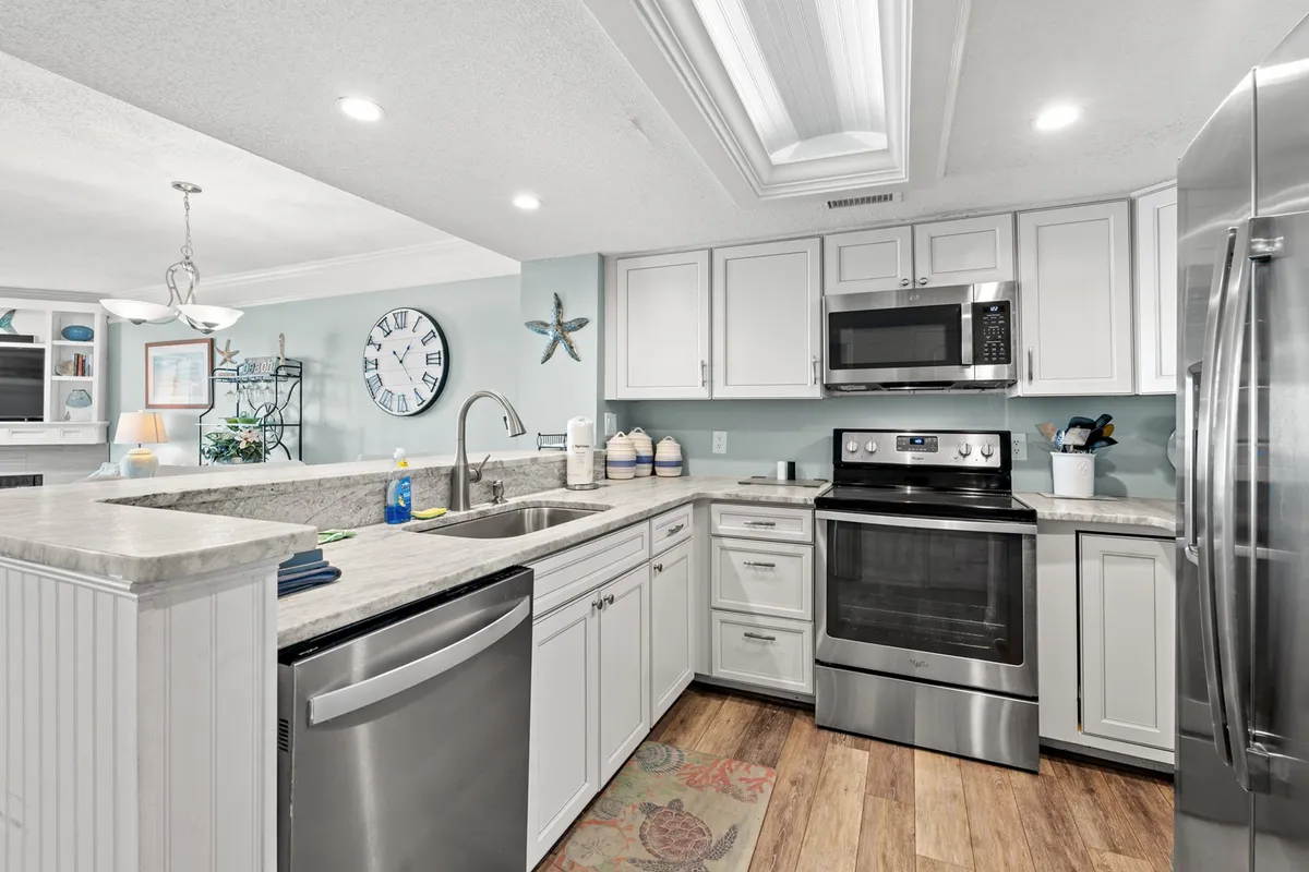 This image presents a warm, inviting kitchen scene featuring a spacious kitchen island, sleek stainless steel appliances, a decorative wall clock, and coastal-themed decor such as a starfish. The setup is clearly designed for both cooking and socializing, with ample counter space and an open layout.