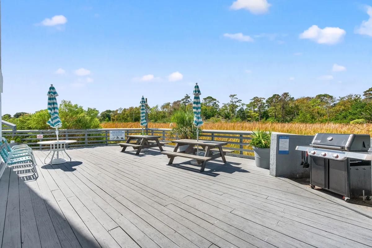 A lively outdoor area with picnic tables, a grill, striped umbrellas, and lush greenery. The space is designed for barbecues, family reunions, and group meals—ideal for casual gatherings across all generations.