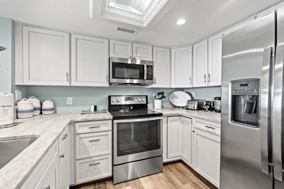 This bright, modern kitchen features stainless steel appliances, a striking granite countertop, white cabinetry, and a skylight that fills the space with natural light. The layout emphasizes room for meal prep and family gatherings, with a clean, practical, and inviting atmosphere.