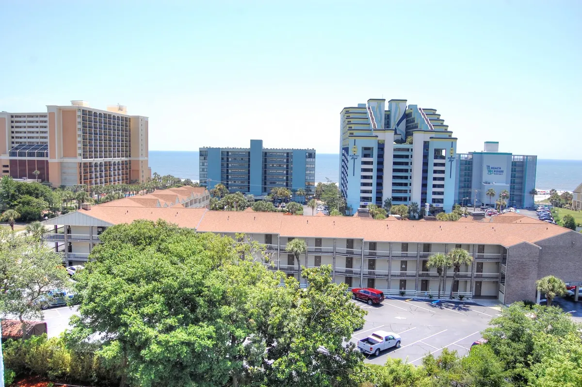This image features a panoramic ocean view framed by lush greenery and modern beachside buildings, suggesting close proximity to both natural beauty and upscale amenities. The scene captures the allure of sunset skies and the vibrant coastal environment, inviting guests to unwind and explore.