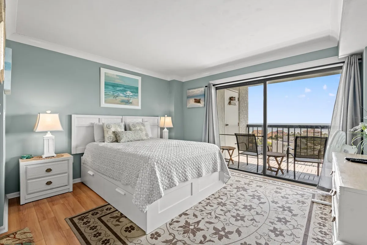 This image features a serene king bedroom with a neatly made bed, flanked by nightstands and illuminated by soft natural light. The room opens up to a balcony view, suggesting a spacious and tranquil retreat ideal for rest and privacy.