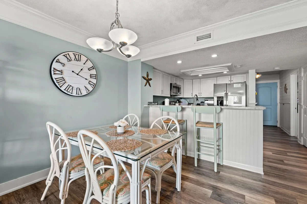 A bright dining area with a table set for meals, a decorative wall clock, a nearby bar area, and accents like a starfish decoration, evoking a cheerful, beach-inspired atmosphere ideal for shared meals and celebrations.